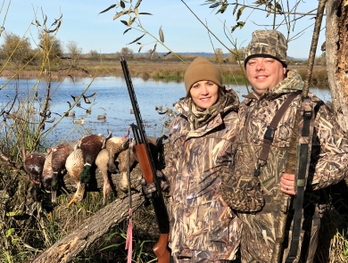 Two duck hunters holding shotguns pose with water in the background at Ridgefield National Wildlife Refuge