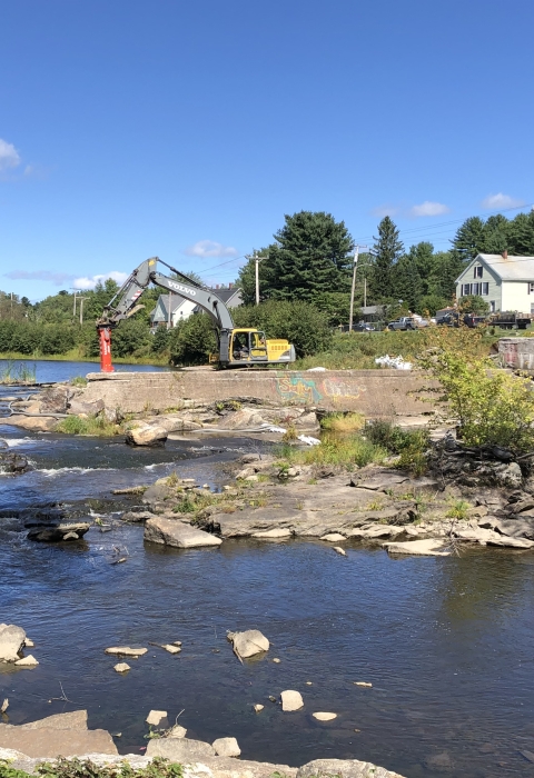 Concrete dam spans halfway across a river with heavy machinery and people in construction hats on top