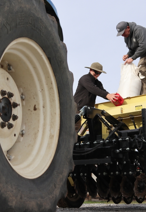 Three people standing behind a tractor loading a seed planter