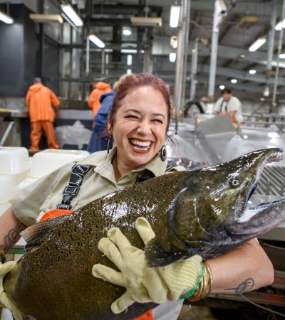 A woman with a huge smile on her face holds a massive salmon in both arms.