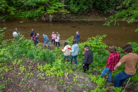 High school students walk down to a river, each carrying a plastic container holding a Big Sandy crayfish.