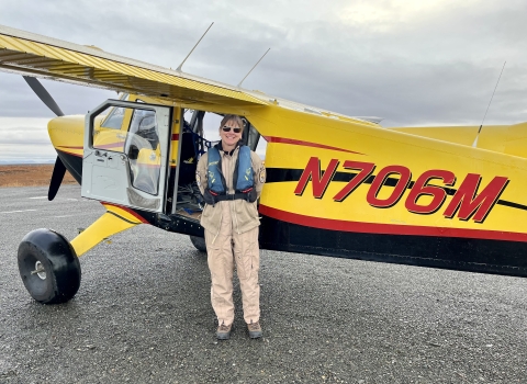 Kara Hilwig standing next to a single engine bush plane on a dirt airstrip.