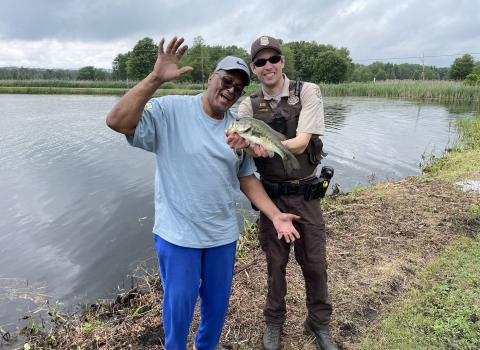 Law Enforcement Officer Mike McMenamin poses with a veteran and the bass he caught at the Veterans' Fishing Derby at Wallkill River National Wildlife Refuge
