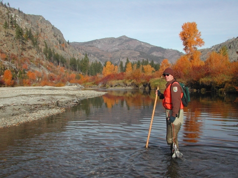 Man in brown uniform stands in river in fall