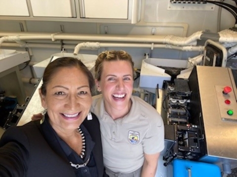 Secretary of the Interior Deb Haaland standing next to Chanice Davies, fish biologist, inside of a marking trailer