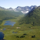 Two small deep blue lakes in a steep, verdant valley with snow-capped mountains in the distance