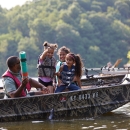 A man is fishing in a boat with three young girls. The kids are excitedly pulling a fish out of the water.