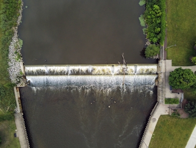 Aerial view of a dam in a dark river with green grass on both side