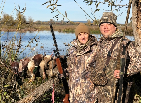 Two duck hunters holding shotguns pose with water in the background at Ridgefield National Wildlife Refuge