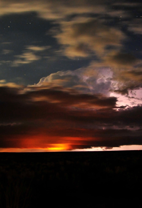 Sunset, stars, and storm clouds converge over a silhouetted landscape