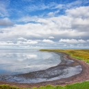 View of a curved green coastline under a cloudy blue sky.