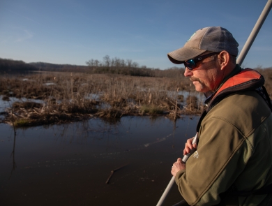 Biologist stands on the front of a boat with net to catch fish.