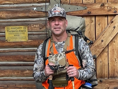 man in camo, orange vest holding hiking poles