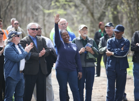 A smiling woman raises her arm high while a group of people standing around her smile at her and applaud.