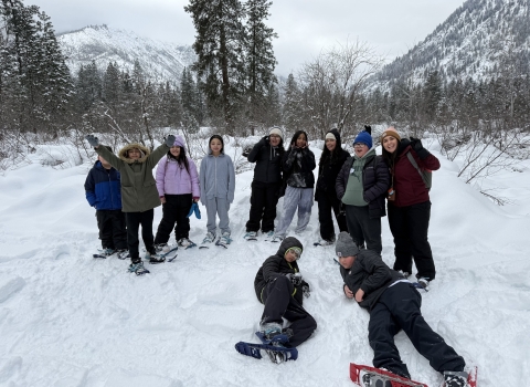 A group of 11 students gathered in snowshoes with mountains behind them