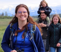 Smiling woman wearing blue SCA uniform leads family on a guided walk.