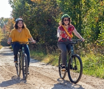 Two woman in bright clothing and helmets riding down a dirt road on electric assisted mountain bikes