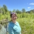 a woman in a blue long sleeve shirt and sunglasses on her head smiles with green field and river in the background