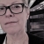 close up of a woman wearing glasses with a spiral staircase behind her