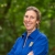 Director Martha Williams stands outdoors, smiling, with arms folded, wearing a blue shirt with FWS logo. Behind her is a wooded area.