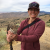 A woman with a hat on is holding a sharp shinned hawk with both hands