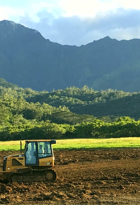 A dozer levels brown earth. Behind it are dramatic green mountains.