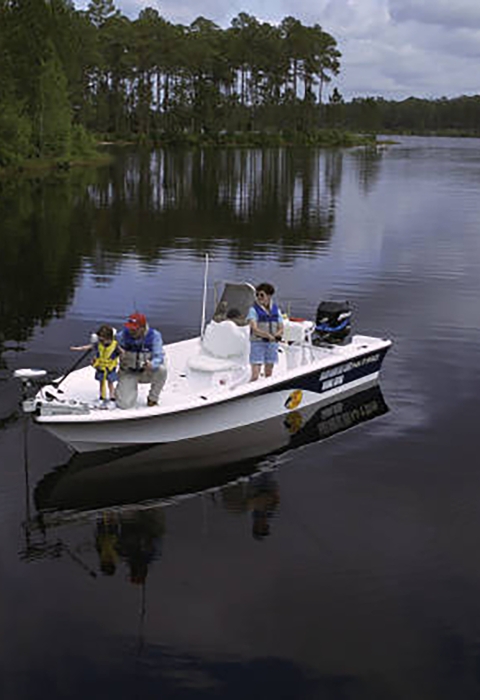 Family fishing in a boat on a body of water with woody landscape in the background. 