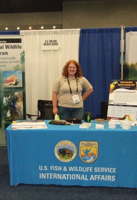 A woman stands behind a table with a tablecloth that reads U.S. Fish and Wildlife Service International Affairs