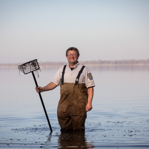 Man stands in water wearing waders as he is holding a net.