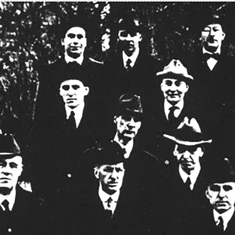 Several men stand in four rows wearing suits and hats.