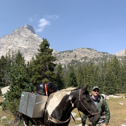 Photo of Mitch Renteria standing next to a horse at the Cirque of the Towers Wyoming.