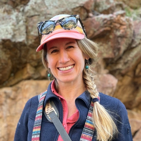 A white woman with braided, blonde hair, wearing a pink hat smiles into the camera