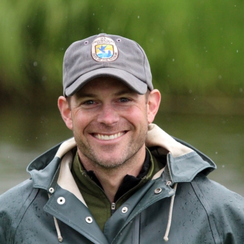 Smiling man wearing a USFWS baseball hat