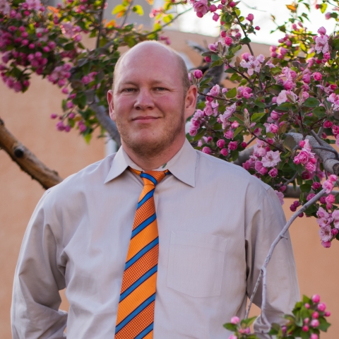 Close up of bald man in tie and shirt with pink apple blossom tree in the backround.