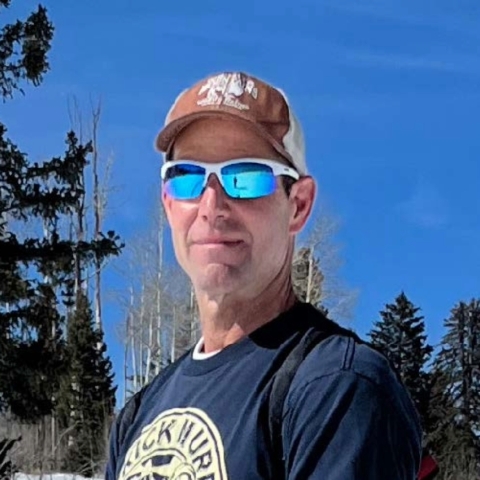 Grant Harris outside in a conifer forest wearing sunglasses.