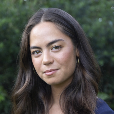 A portrait of a woman with brown hair just below the shoulders. She is in a blue shirt against a green background. 