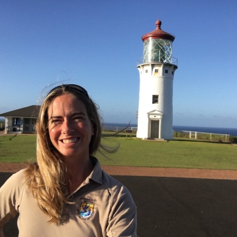 woman wearing USFWS uniform stands near a lighthouse