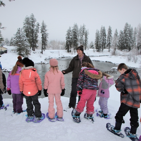 A FWS employee stands with a group of young students in snow gear with Icicle Creek and a snow covered landscape in the background