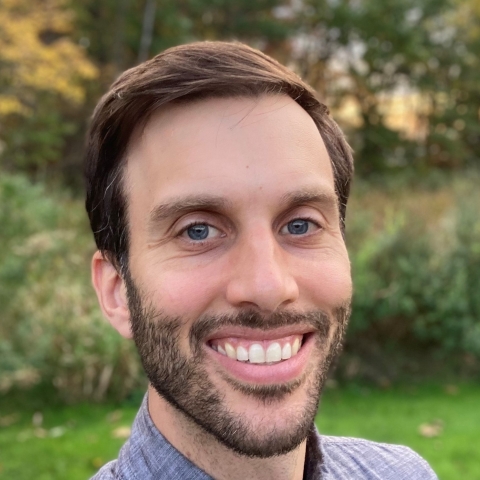 a headshot of a man with brown hair and a short beard outside