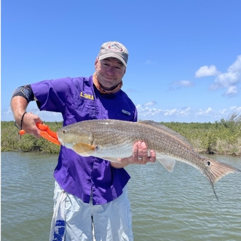 Jeff smiling holding a large fish in white shorts and a blue jacket