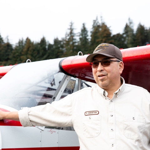 Man in USFWS uniform stands with one hand on the nose of a small red and white plane