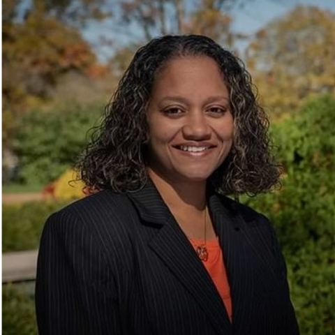 Lorisa smiles in a black blazer and orange blouse 