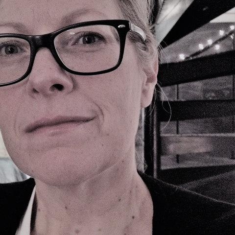 close up of a woman wearing glasses with a spiral staircase behind her