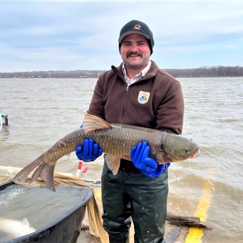 Man in fws uniform holding fish and smiling