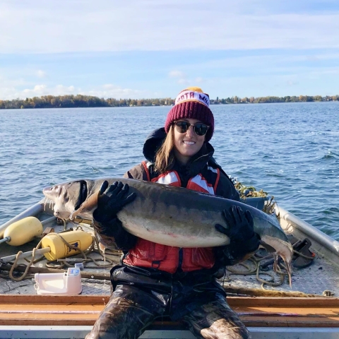 Woman sits on boat and holds big fish