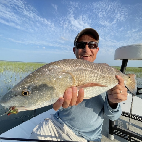 a man wearing a hat and sunglasses holding a fish in a boat