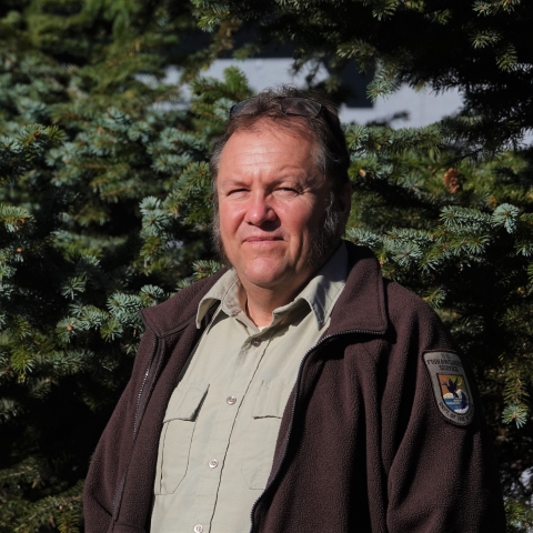 man in usfws uniform stands in front of a spruce tree