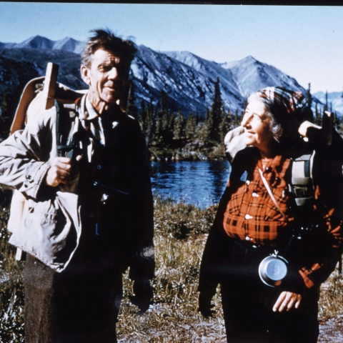 man and woman standing with backpacks with mountain in background