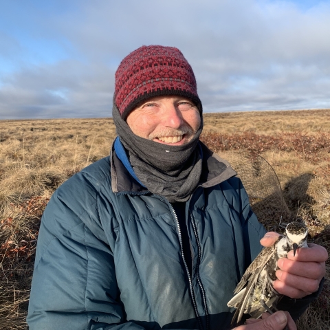 Rick Lanctot smiles and holds a tagged bird outdoors.