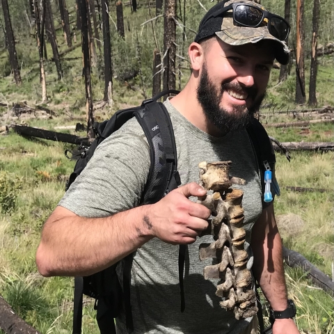 a man holding up an animal bone in the woods